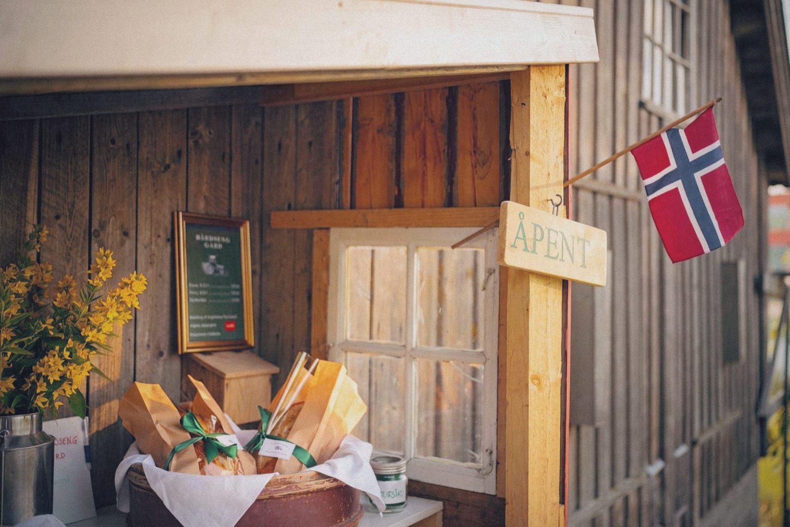 The Baardseng Gård farmstand, a small wooden hut with the Norwegian flag flying beside it in the meadow.